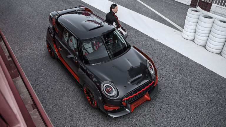 Man is leaning with his back against the door of a red and black MINI John Cooper Works Concept.