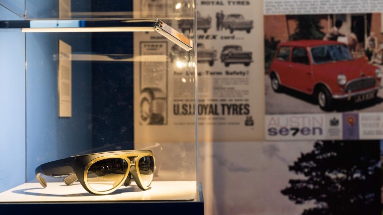 Gold racing glasses with a built-in camera are displayed in a glass case.