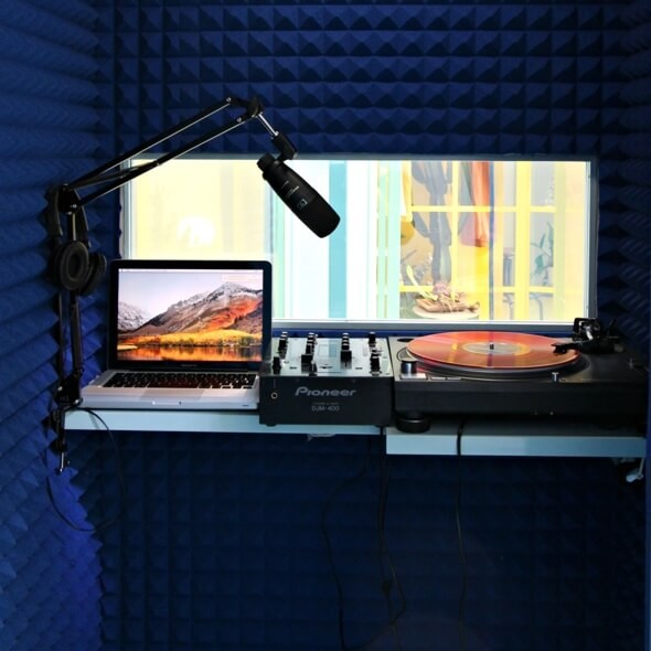 Blue soundproofing foam lines a tiny recording studio with a microphone and vinyl turntable.