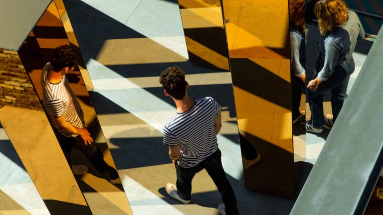 People walk through a series of yellow mirrored columns.