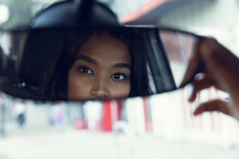 Young woman altering her rear-view mirror while driving.