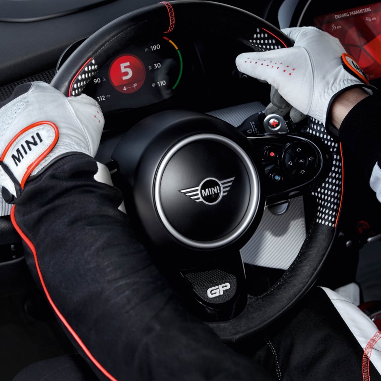 A man in racecar driving gear has his hands on the wheel of a MINI John Cooper Works Concept.