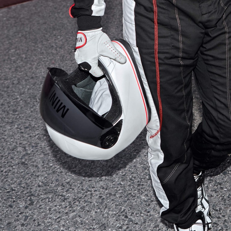 A man in racecar driving gear stands behind a red and black MINI John Cooper Works Concept.