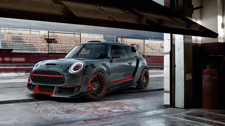 A red and black MINI John Cooper Works Concept, seen from the side, is parked in front of the stands at a race track.