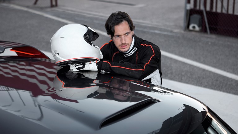 Cool, young man in racecar driving gear leans on the roof of his MINI John Cooper Works Concept.