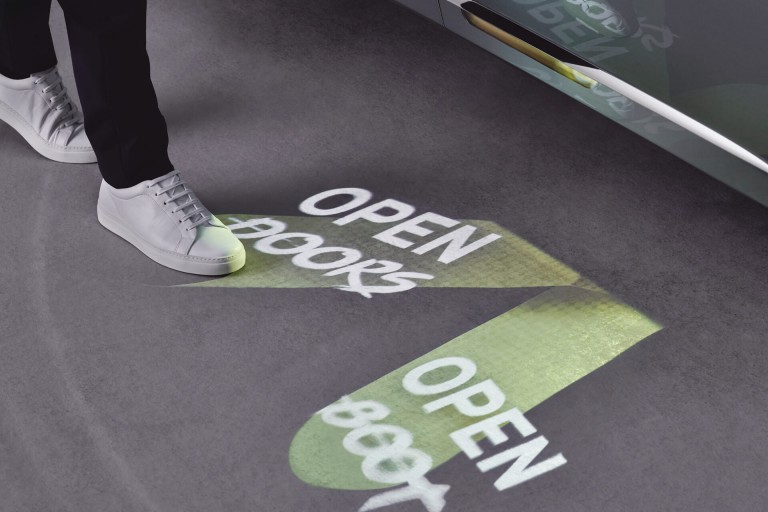 Projected foot controls on the ground beside a MINI VISION NEXT 100 – OPEN DOORS, OPEN BOOT. 
