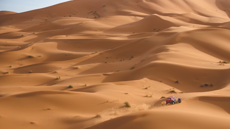 A tiny MINI ALL4 Racing car almost disappears in what seems like endless sand dunes.