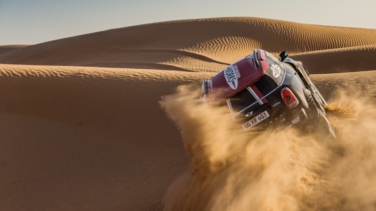 MINI John Cooper Works Rally car leaves a cloud of sand in its wake while tearing up a dune.