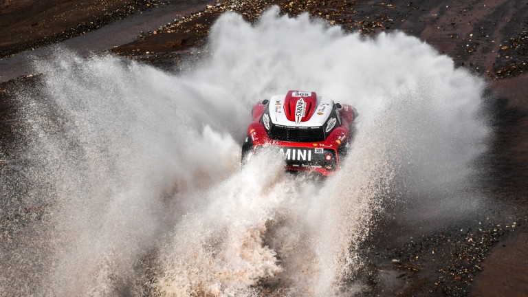 Overhead view of the MINI John Cooper Works Buggy driving through water, sending a jet of spray into the air at the Dakar Rally 2018.