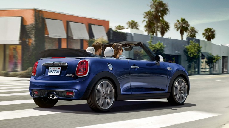 MINI Convertible driving along a coastal road in the sunshine with top folded down.