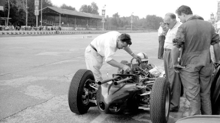 Motorsport pioneer John Cooper attending to the engine of a Mk 1 racer, trackside. 