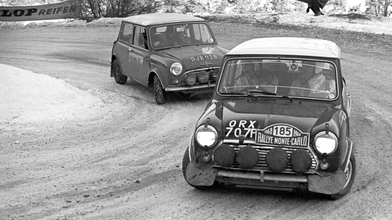 The BMC Works Mini Cooper S comes around a snowy turn, followed closely by another car, at the 1965 Monte Carlo Rally.