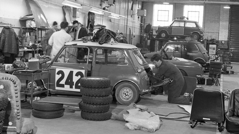 A Mini Cooper racer is being worked on in a garage by a pit crew.