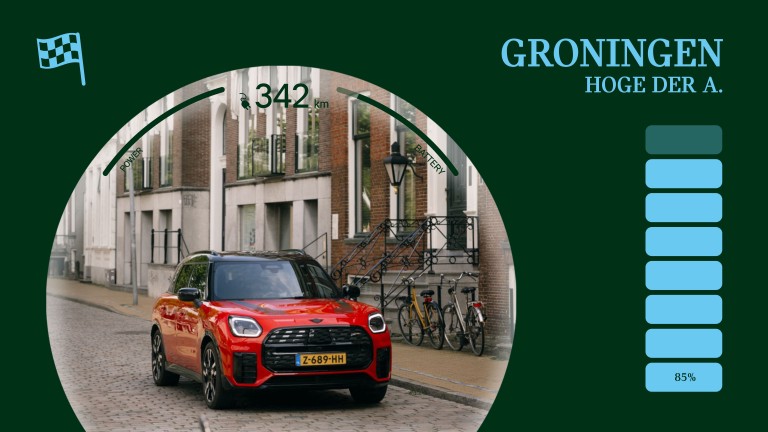 Pictured from the front, the all-electric MINI Countryman in Chili Red with roof in black driving down a street in the Dutch city of Groningen.