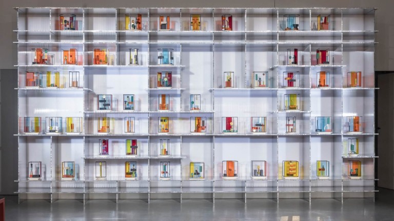 A large white shelf unit full of colourful, abstract totem models