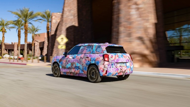 MINI Aceman with camouflage driving down a street, seen from the side.