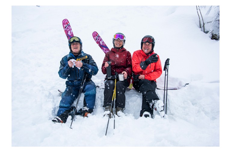 Image of three “Silver Sliders”, who are sitting in the snow with their ski equipment. rope, while another skis.