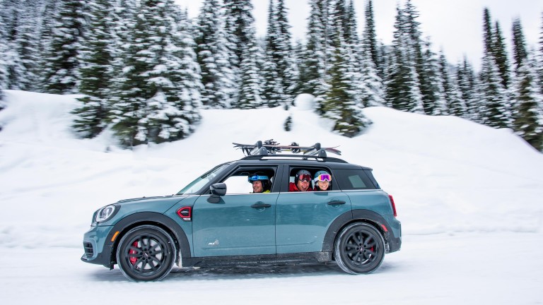 Image of a MINI Countryman in a snowy landscape, with members of a skiing group looking out of the window. 