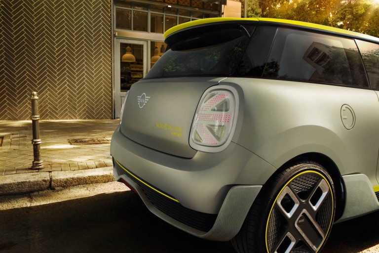 The tail-end of a silver and yellow MINI Electric Concept car is seen parked in front of a retro-looking shop.