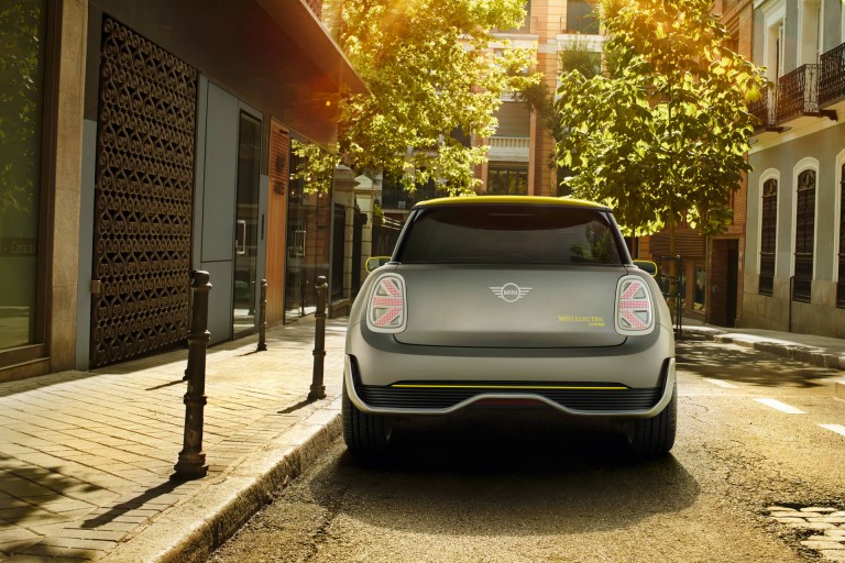A silver and yellow MINI Electric Concept car, shown from the rear, is parked in a sunny city street.