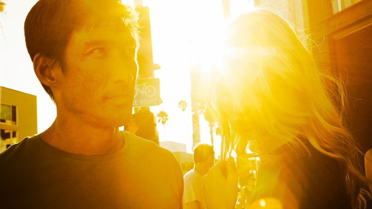 Street scene showing a close-up of a young woman and young man with electrifying sunshine shining behind them. 