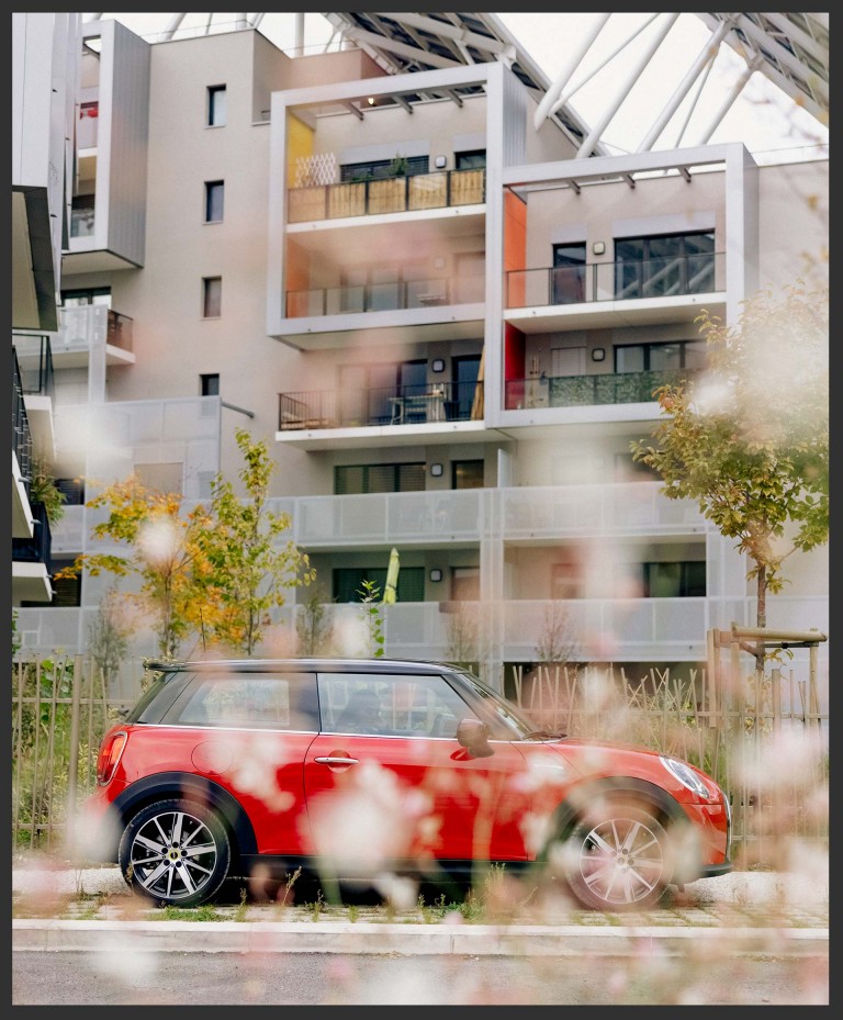 Image of the MINI Cooper SE in Chili Red, in front of Résidence ABC, Grenoble, France. 
