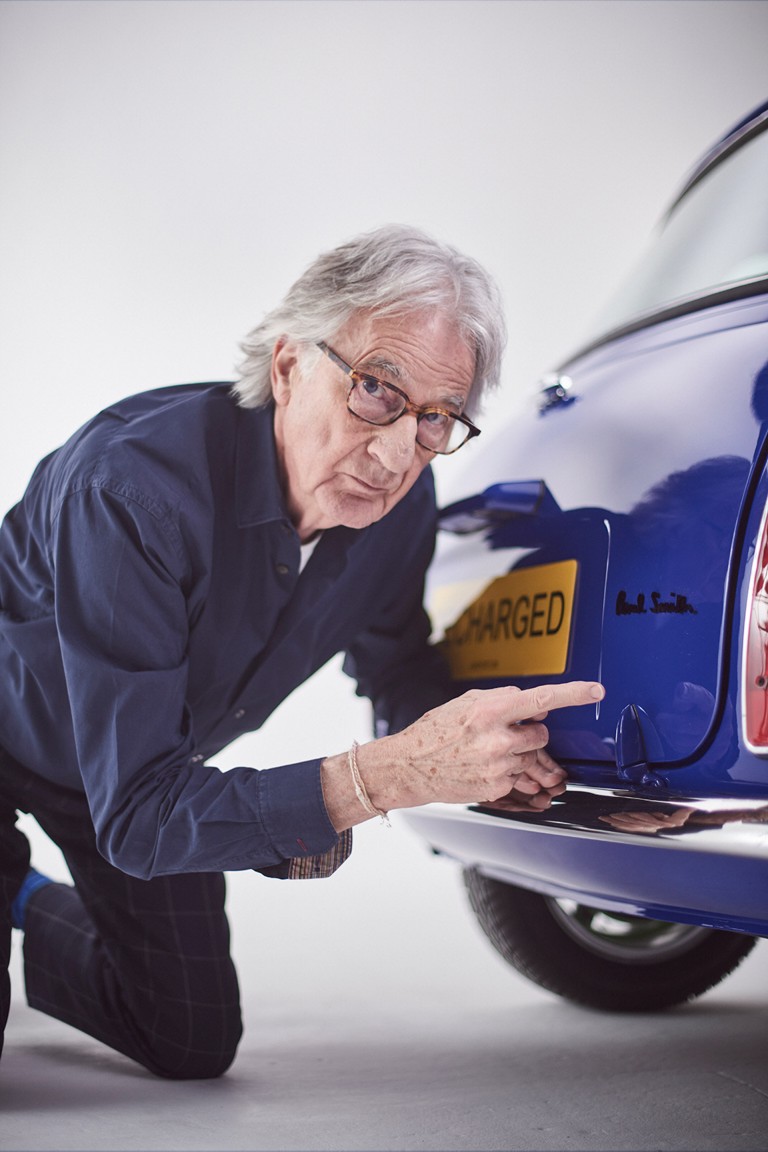 Paul Smith kneels and points at his logo on the back of the blue MINI Recharged model. 