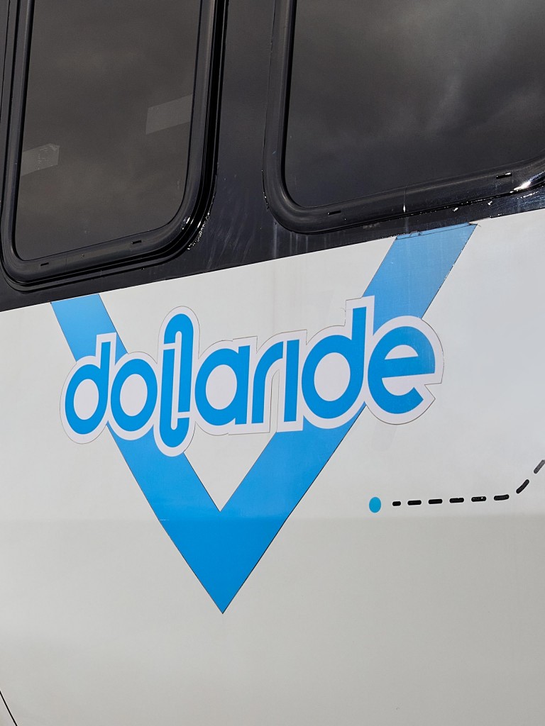Alt-tag:  Close-up of the company’s logo in blue and white on a Dollaride van.  