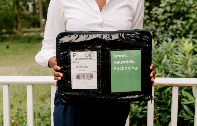 Chantal Emmanuel holds one of her reusable packages with a prepaid label into the camera.
